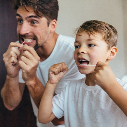 Father and son flossing their teeth in bathroom